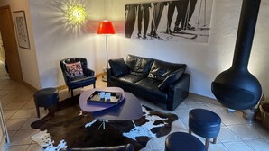A living room with a black leather sofa, a red floor lamp, a cowhide rug, and a black and white artwork on the wall. - Superb 70M2 apartment, fireplace, terrace, pool/spa and private shuttle service  (Champagny-En-Vanoise)