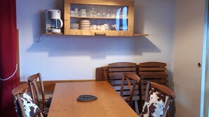 Un coin repas avec une table et des chaises en bois, un luminaire suspendu et des étagères au-dessus pour ranger les ustensiles de cuisine.