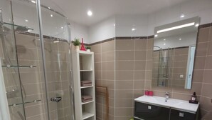A modern bathroom with a glass-enclosed shower, a vanity with a mirror, and a green rug on the floor. - Charming cottage by the Seine (Villeneuve-le-Roi)