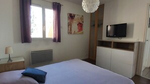 A bedroom with a large bed, a TV on a stand, a radiator, and a window with curtains. - Charming cottage by the Seine (Villeneuve-le-Roi)