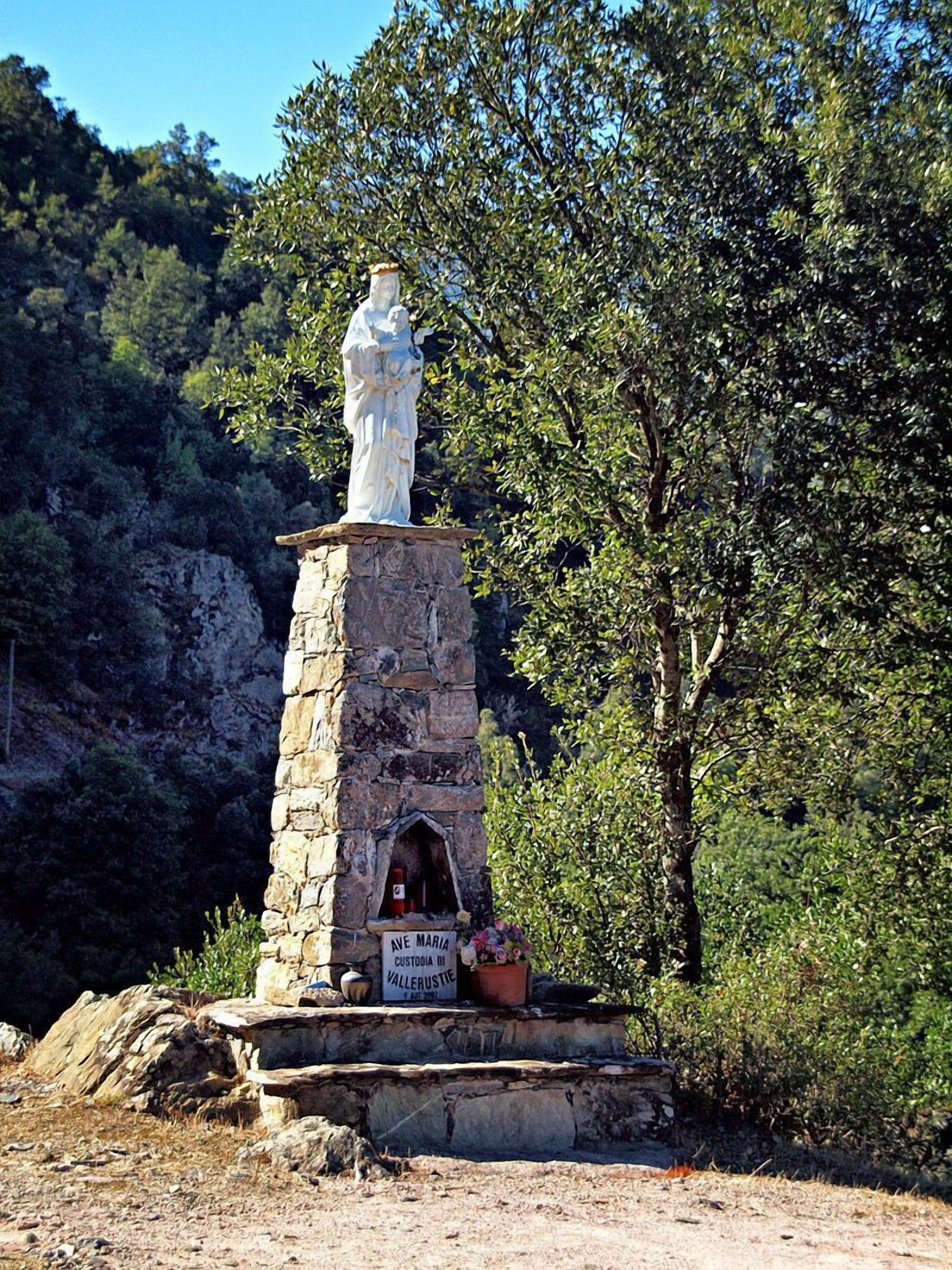 A stone monument with a statue, a plaque, and a small archway.