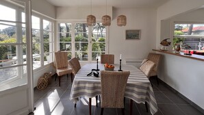 A dining area with wicker chairs, a striped tablecloth, and a view of greenery outside.