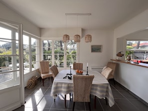 A dining area with wicker chairs, a striped tablecloth, and a view of greenery outside.