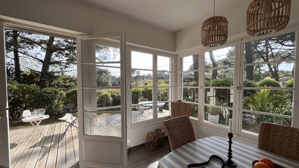A sunlit room with large windows, a wooden deck, and outdoor furniture.