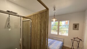 A bedroom with a bed, a window, a radiator, a hanging light fixture, and a wooden partition.