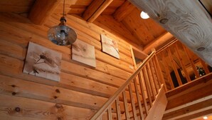 A wooden staircase with a metal handrail leading to a loft area with wooden beams and a hanging light fixture.