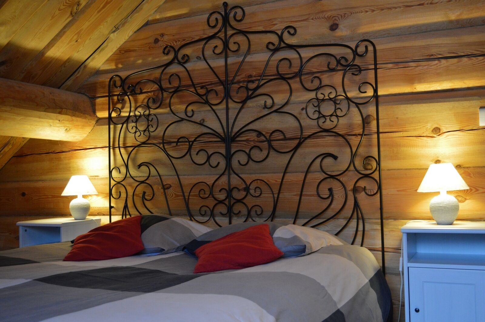 A cozy bedroom with a decorative metal headboard, a bed with multiple pillows, and two bedside lamps on white nightstands.