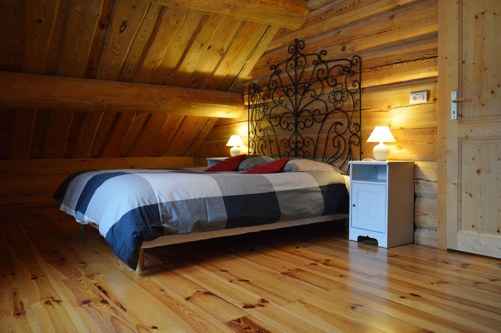 Un dormitorio acogedor con techo de madera, una cama con colcha a cuadros, dos lámparas de noche y una mesita de noche blanca.