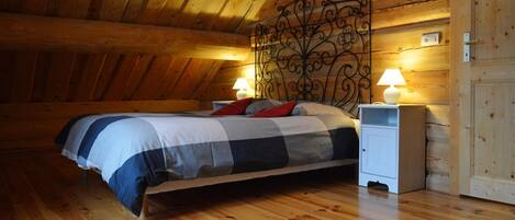 Un dormitorio acogedor con techo de madera, una cama con colcha a cuadros, dos lámparas de noche y una mesita de noche blanca.