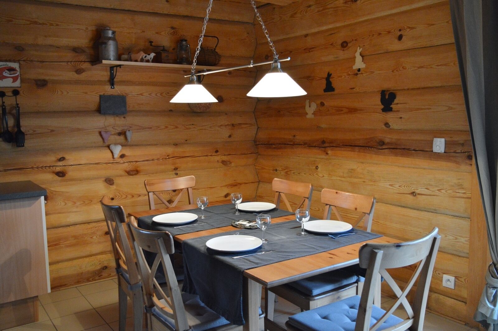 Comedor de cabaña de madera con una mesa preparada para cuatro, sillas y lámparas colgantes.