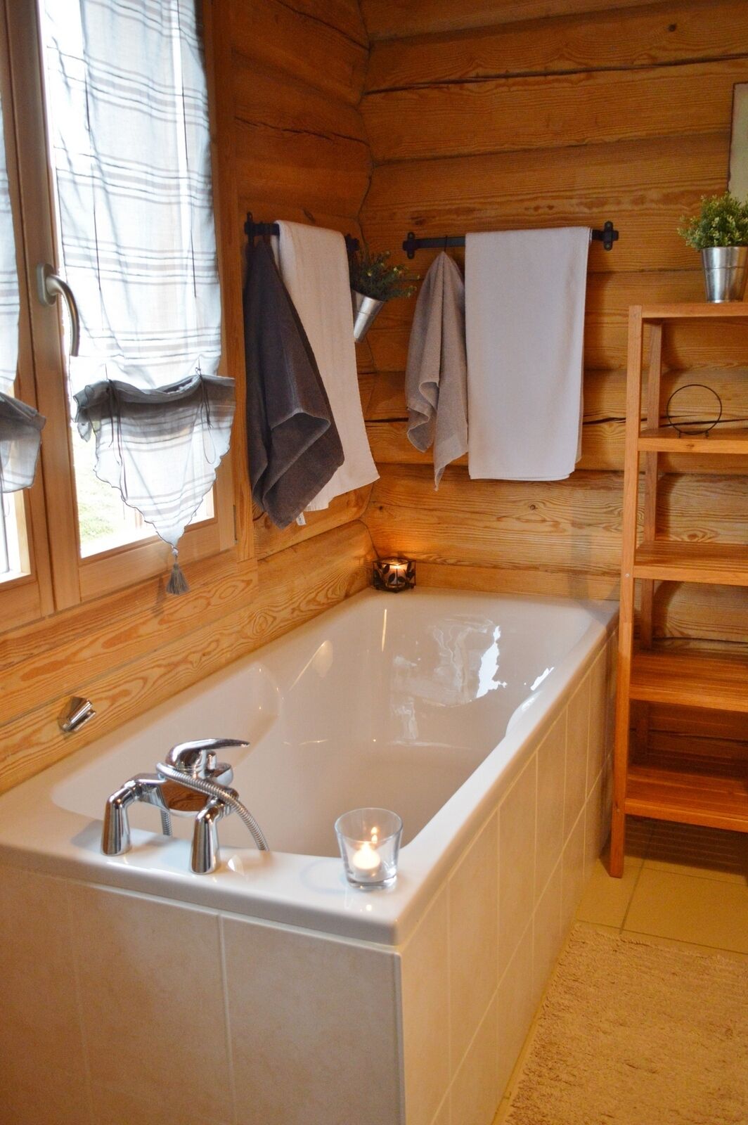 Un baño de cabaña de madera con una bañera, un estante con toallas y una pequeña planta.