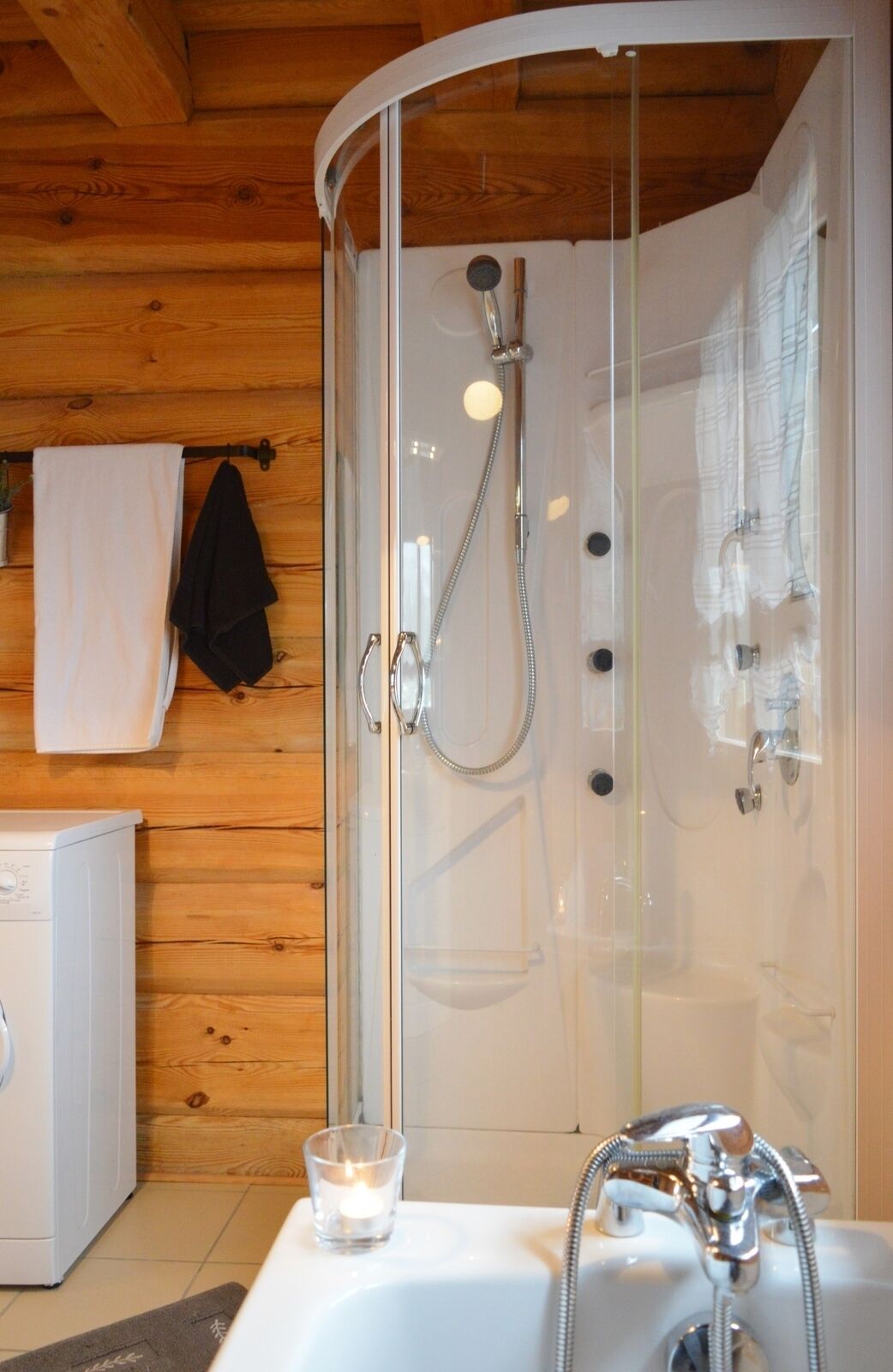 A modern bathroom with a glass-enclosed shower, a white sink, and a washing machine.