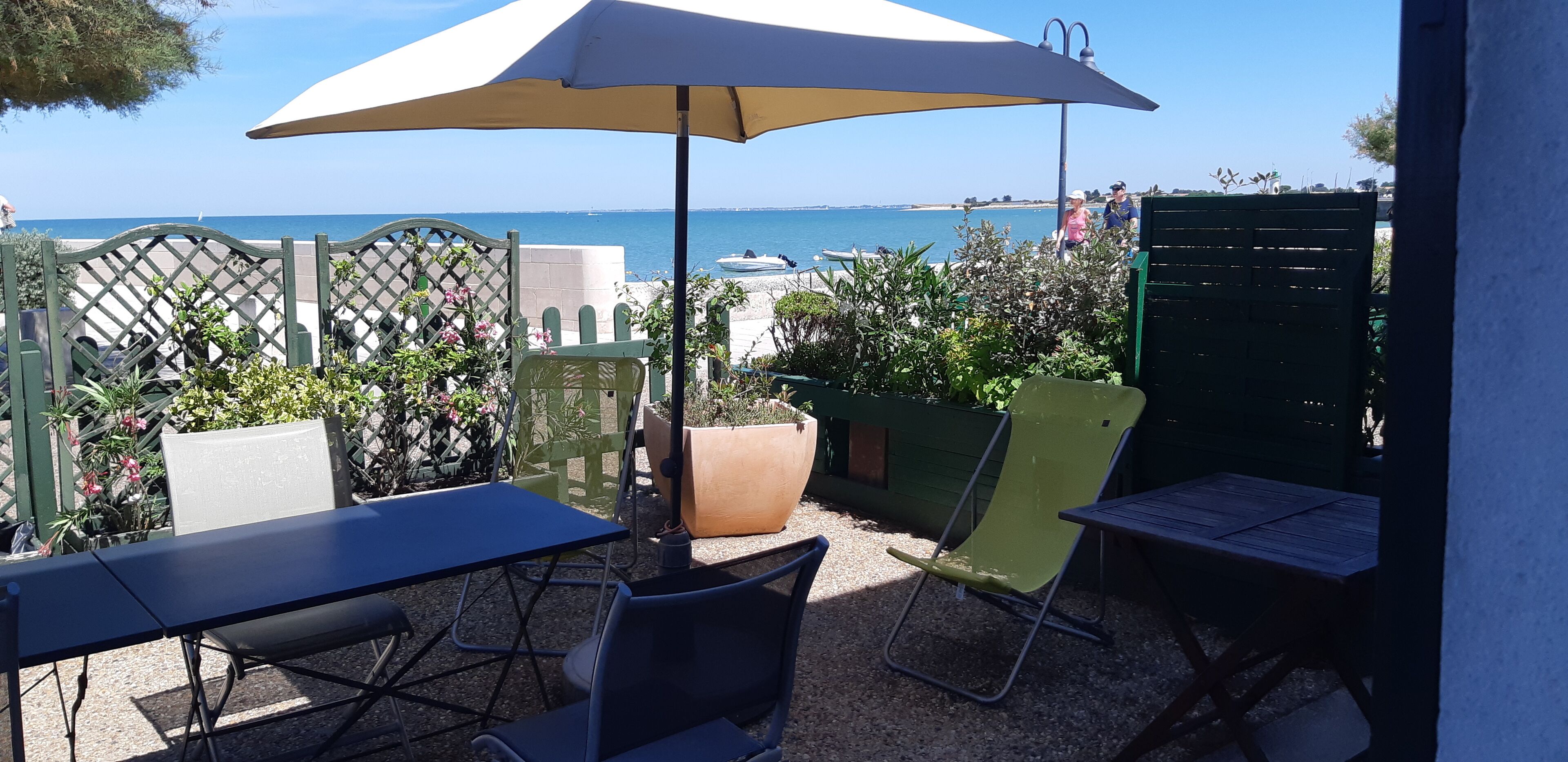 An outdoor patio with a table, chairs, and an umbrella, overlooking a beach and sea.