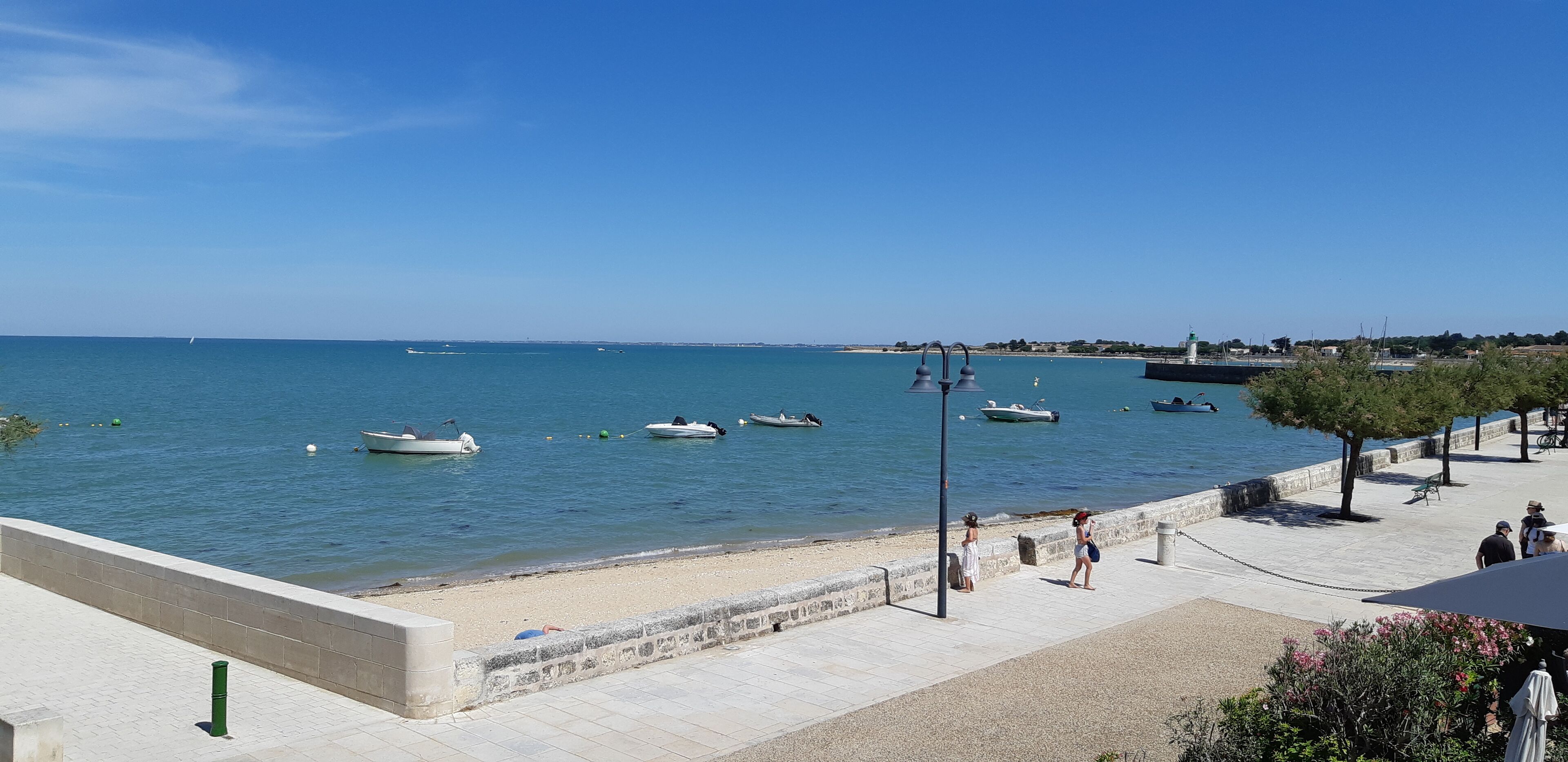 Un paseo marítimo con vista despejada al mar, barcos y una costa lejana.