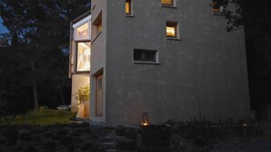 A modern building with multiple windows, a visible entrance, and a small outdoor light fixture. - Architect house in Provence (La Roque-Alric)