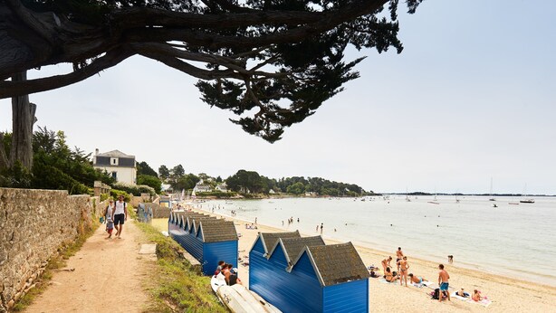 A beach with blue beach huts, a stone wall, and a clear view of the sea.