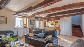 A spacious living room with a leather sofa, a coffee table with various items, and exposed wooden beams on the ceiling.