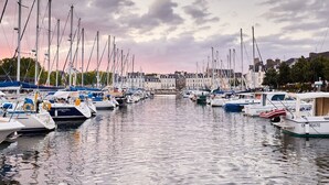 A marina with numerous boats docked, a bridge in the background, and buildings along the waterfront.