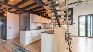 Une cuisine moderne avec des meubles blancs, un îlot central en bois et un escalier doté d’une structure en métal noir.