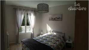 A bedroom with a bed, a bedside table, a lamp, a window with curtains, and a painting on the wall.