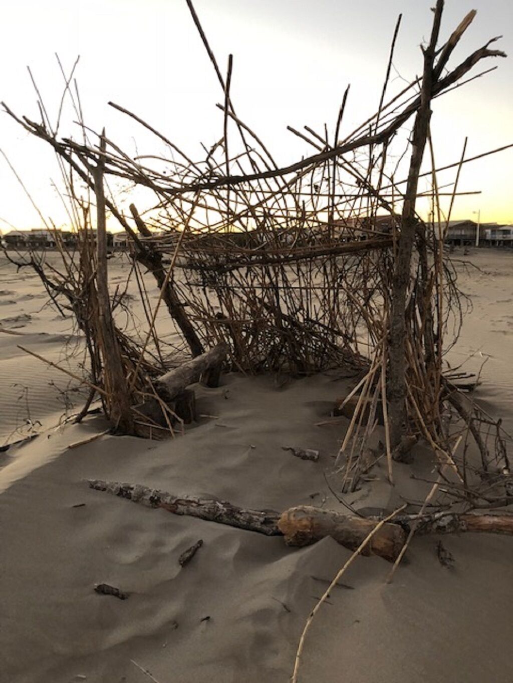 Een constructie van takken en hout op een zandstrand.