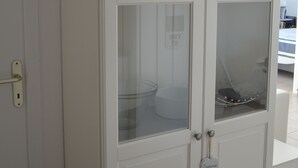 Ett vitt skåp med glasdörrar där köksredskap förvaras.