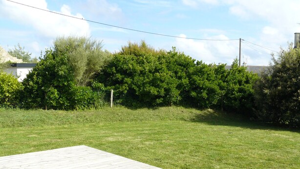 A grassy backyard with a wooden deck. - Single storey house, enclosed land 400 m from the beach of pors-Carn (Penmarch)