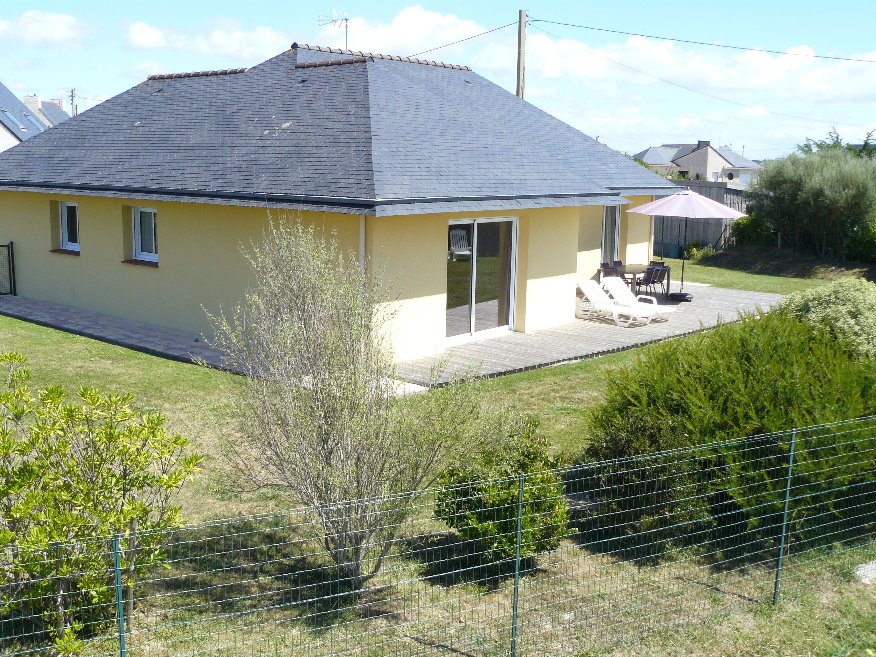 A single-story house with a dark roof, a yellow facade, and a small patio area with outdoor furniture.