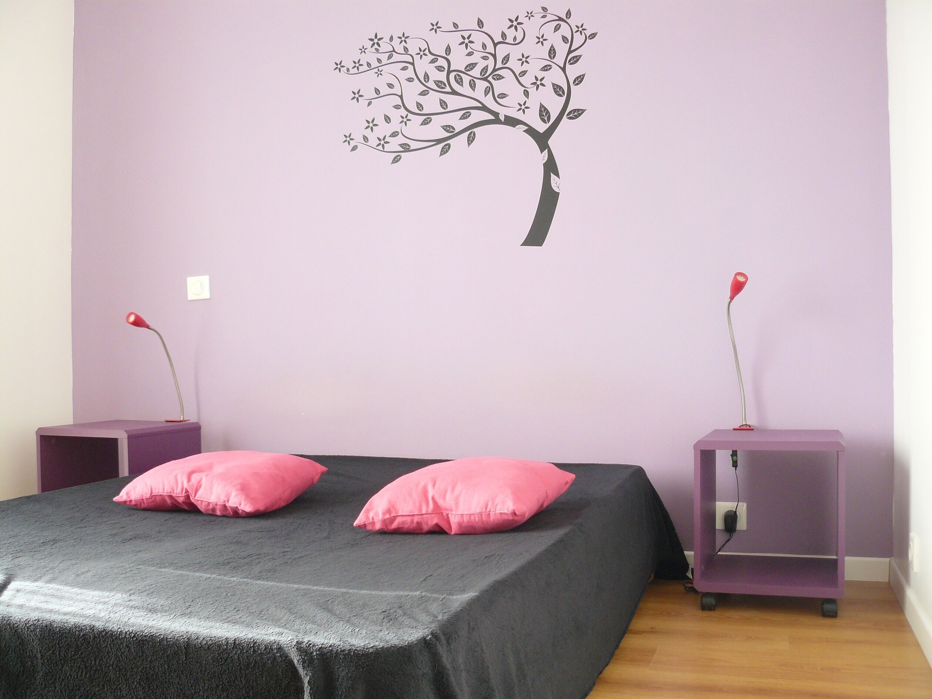A bedroom with a bed, two nightstands, and a wall decoration of a tree.