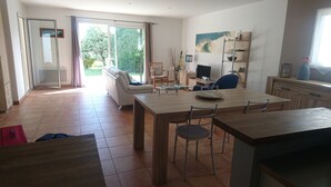 A modern living room with a dining area, a TV, and a large window with a view of greenery. - Single storey house, enclosed land 400 m from the beach of pors-Carn (Penmarch)