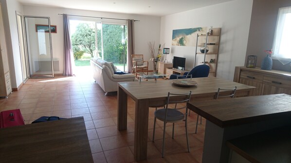 Una sala de estar moderna con comedor, televisor y un amplio ventanal con vistas a zonas verdes.