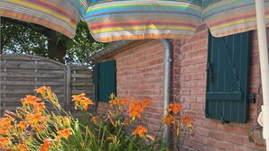 Une terrasse agrémentée de parasols à rayures, d’un mur en briques et de fleurs oranges.