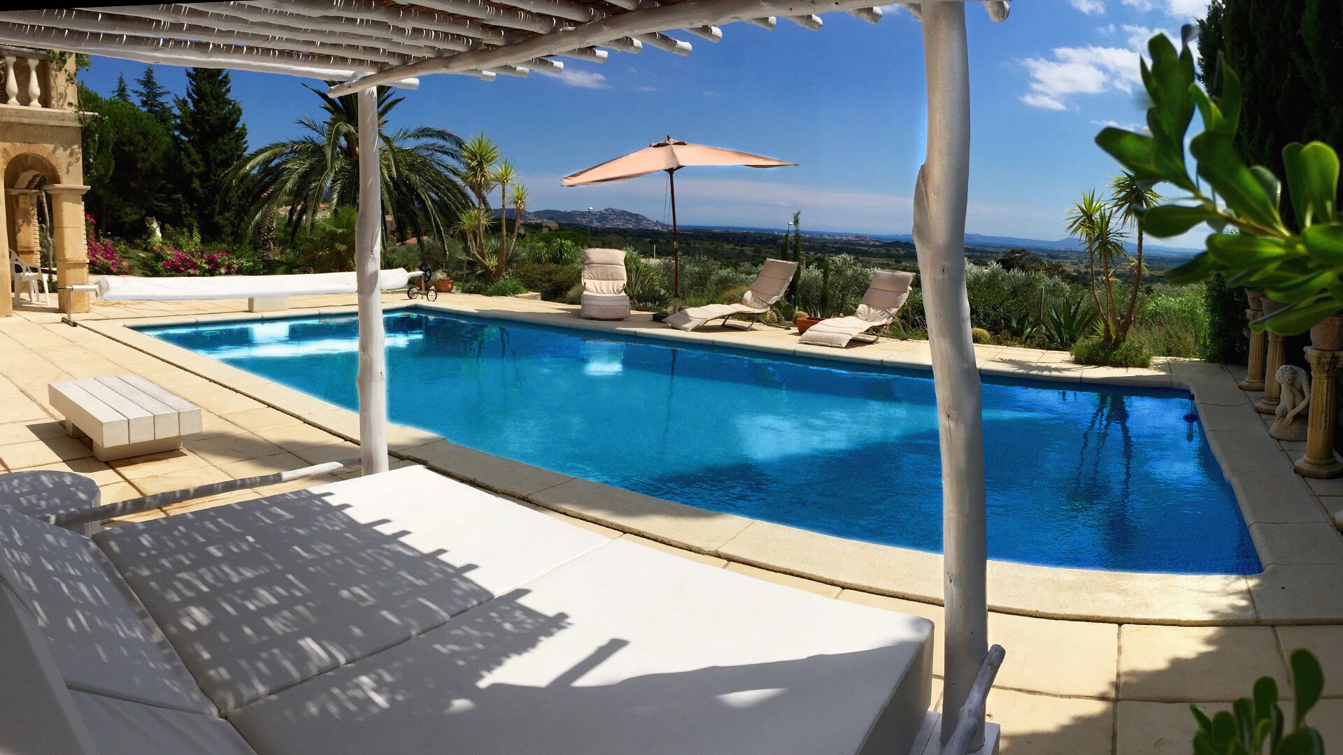 Piscina con sillones de descanso y una sombrilla, rodeada de follaje y vistas al paisaje.