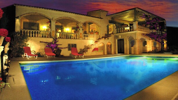 A large house with a swimming pool, red chairs, and a balcony.