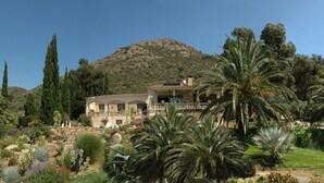A large, multi-story building with a Mediterranean architectural style, surrounded by lush greenery and palm trees.