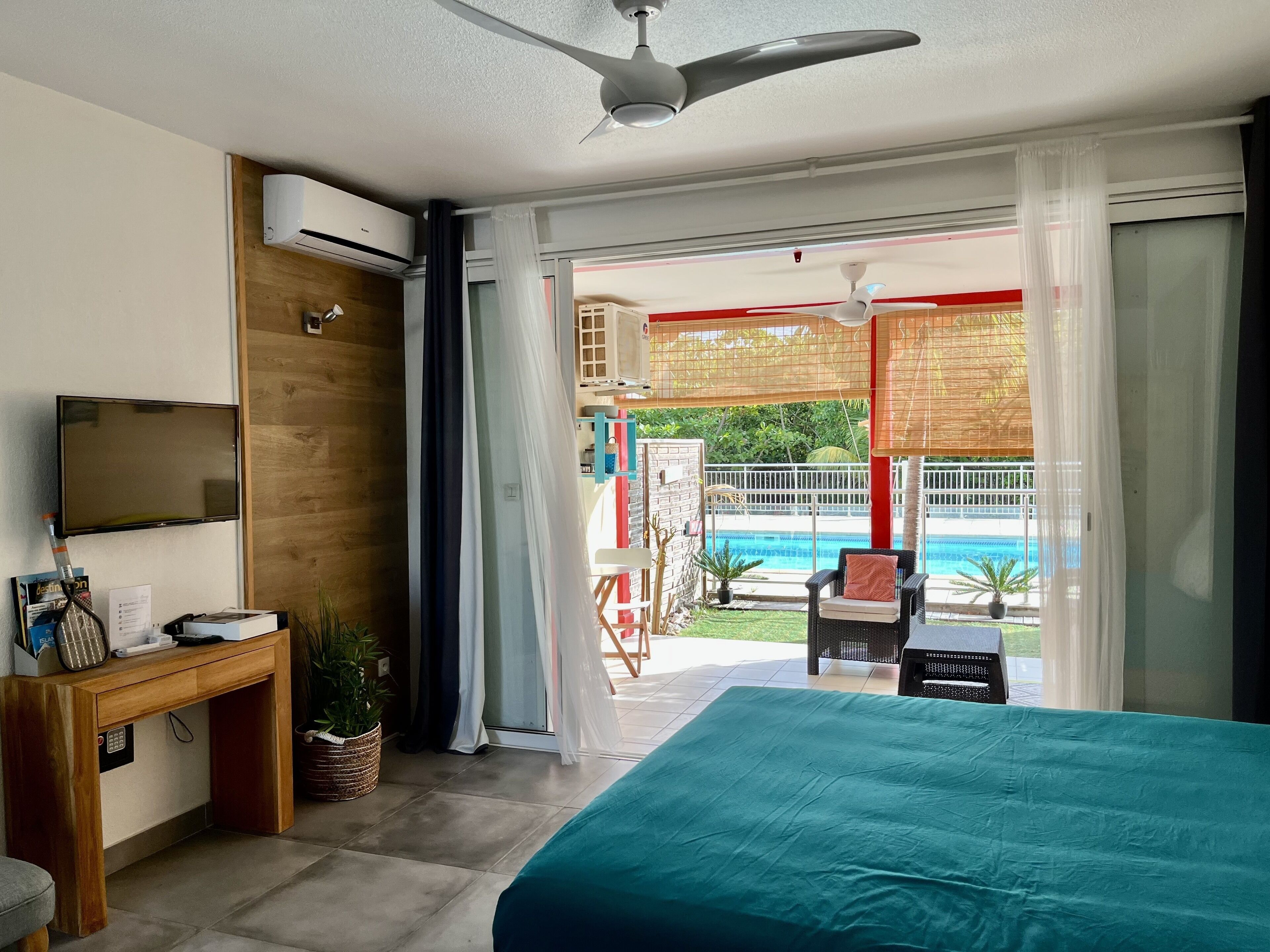 A hotel room with a bed, a desk, a TV, and a view of a pool and outdoor area.