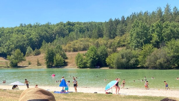 Een strand met mensen die zwemmen en zonnebaden, omringd door een bebost gebied.