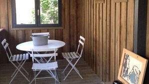 Ein Zimmer mit rundem Tisch und vier Stühlen, ein Fenster mit Blick auf Grünflächen, Holzwände und eine Decke mit weißen Balken.