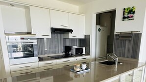 A modern kitchen with white cabinets, stainless steel appliances, and a glass display case with decorative items. - Luxury apartment with splendid sea view (Case-Pilote)