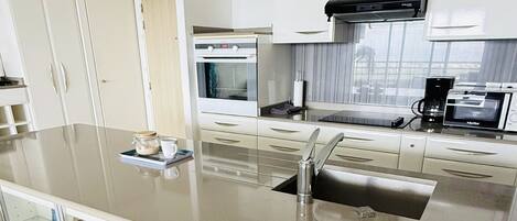 A modern kitchen with a central island, stainless steel appliances, and a glass-fronted cabinet with decorative items.