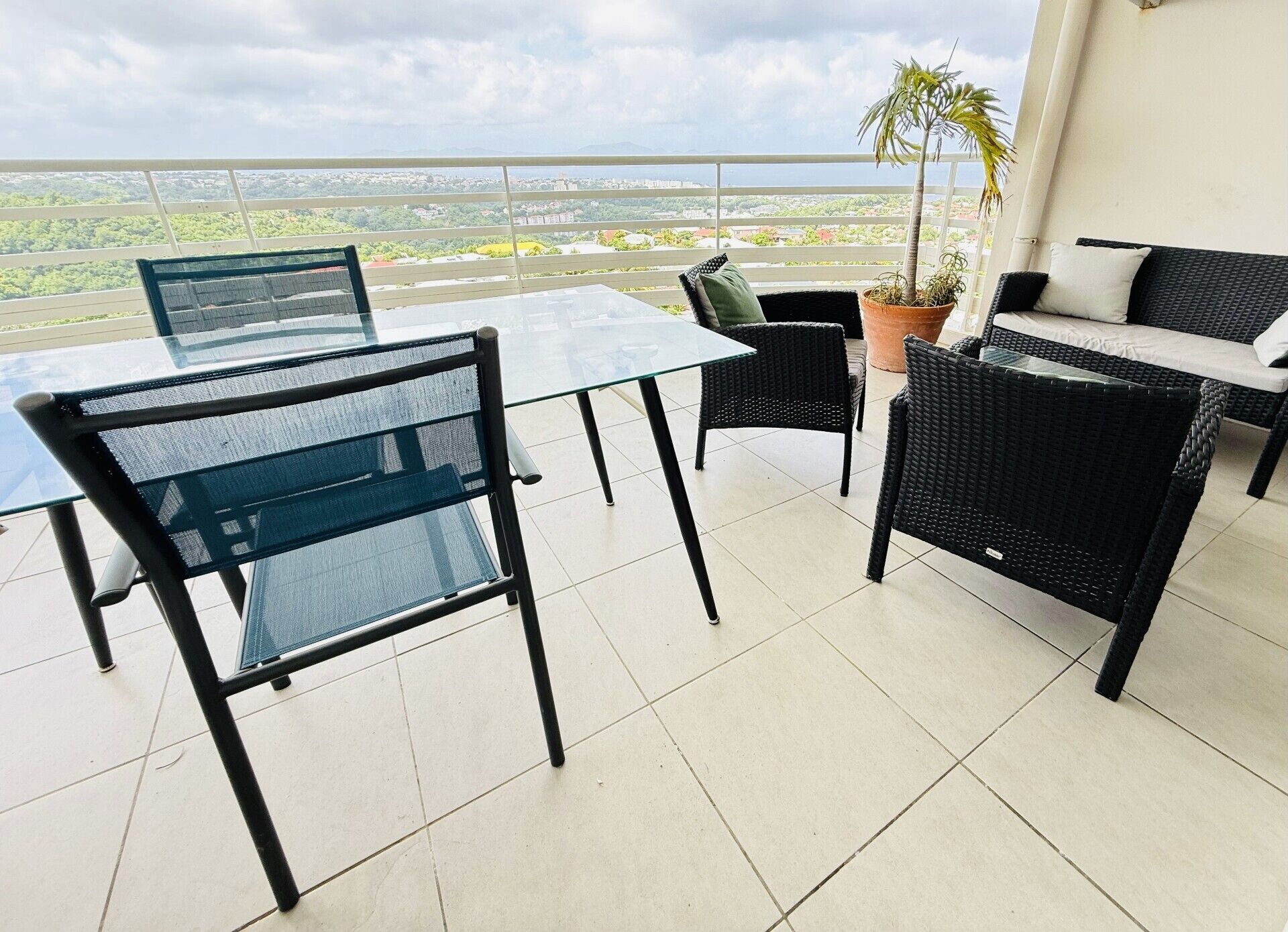 A balcony with a glass table and chairs, a potted plant, and a view of a cityscape.