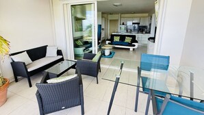 A modern living area with a glass table, wicker chairs, a sofa, and a kitchen in the background. - Luxury apartment with splendid sea view (Case-Pilote)