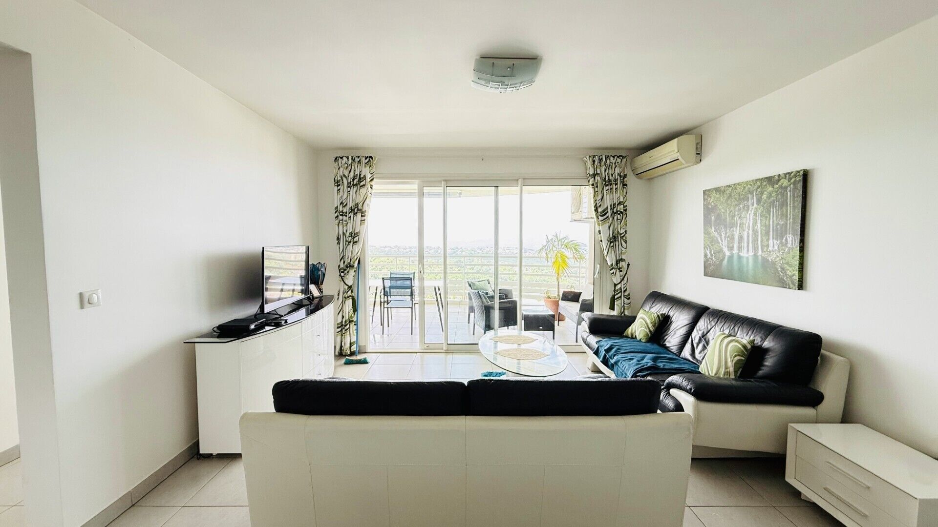 Ein modernes Wohnzimmer mit einer Couch, einem Couchtisch und einem Fernseher. Eine Glastür führt auf einen Balkon.