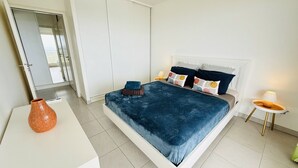 A modern bedroom with a large bed, a white wardrobe, and a small table with a lamp. - Luxury apartment with splendid sea view (Case-Pilote)