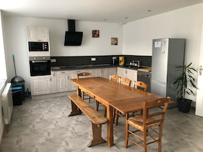 Une cuisine moderne avec des meubles blancs, une table à manger en bois et un four encastré.