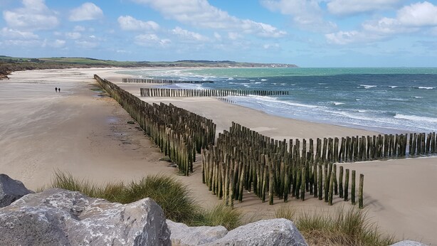 Ein Strand mit Holzstakiten, sandigem Ufer und Wellen.
