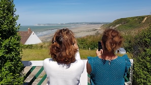 Zwei Personen blicken auf eine Küstenlandschaft mit Meerblick und fernen Hügeln.