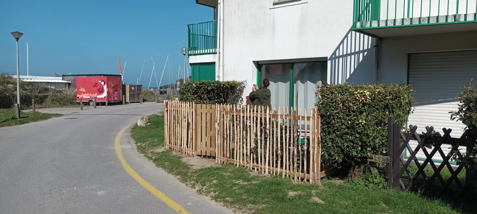 Une route avec une ligne jaune, un camion rouge et un immeuble doté d’un balcon vert.