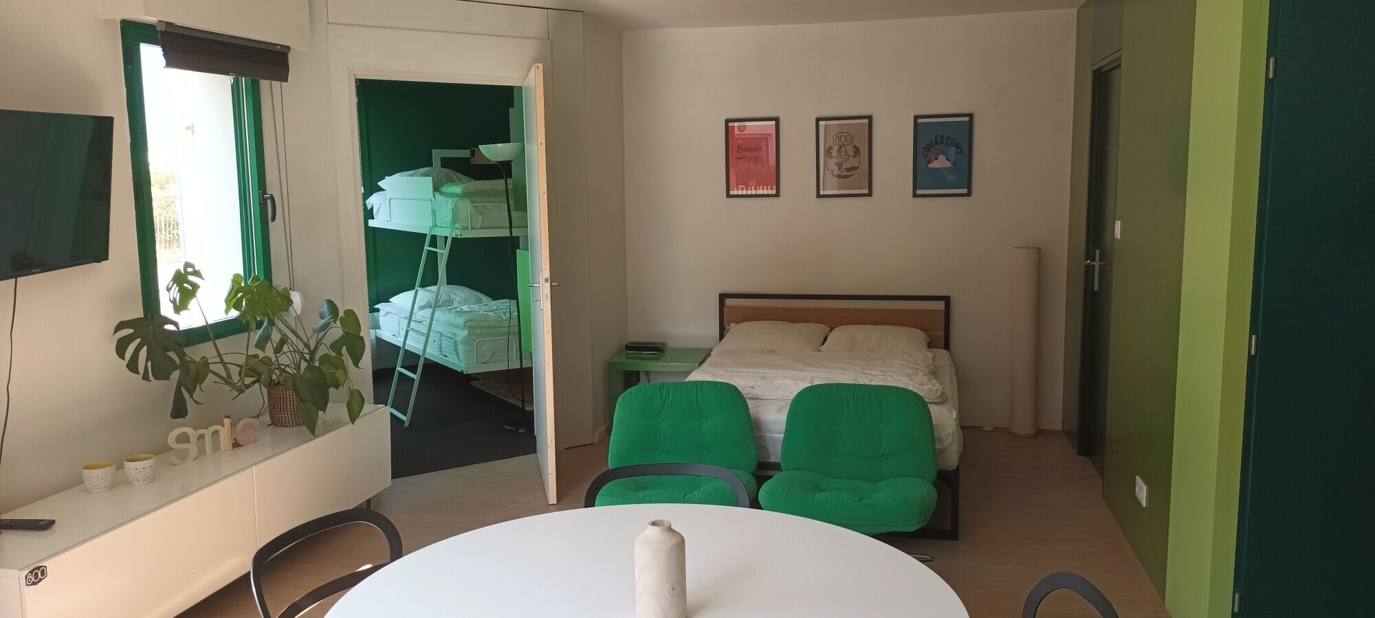A room with a bunk bed, a desk with a chair, a table, and a potted plant.