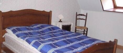 Un lit simple avec un cadre en bois et une couvre-lit à rayures bleues et blanches, dans une pièce aux murs blancs et au plafond en pente.